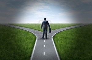 10609226-business-man-at-a-cross-roads-standing-at-a-horizon-with-grass-and-blue-sky-showing-a-fork-in-the-ro